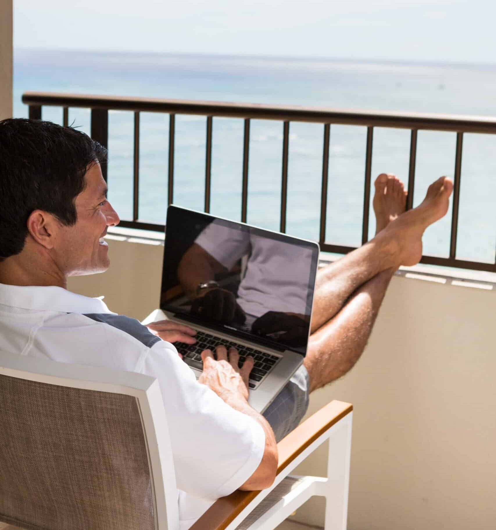 man working on a laptop computer with his feet up in front of an ocean view
