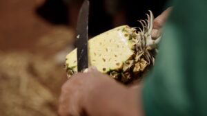A man slicing the skin off a pineapple.